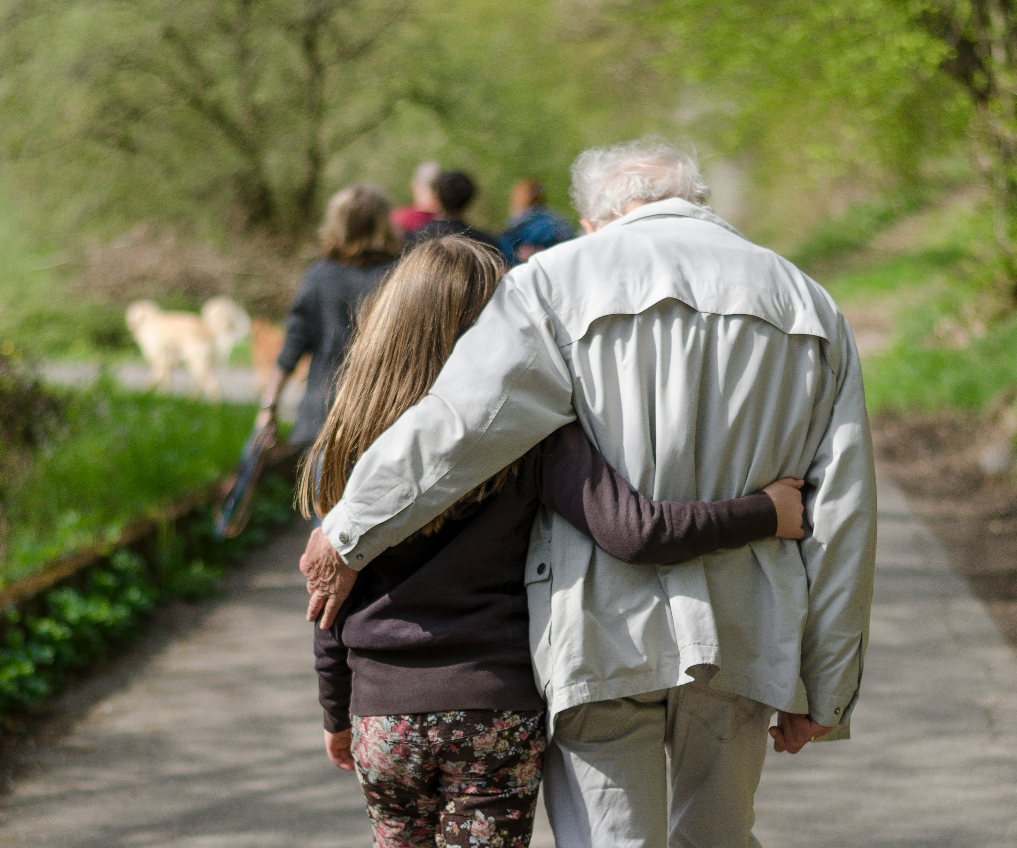 A younger and an eldery person are walking arm in arm