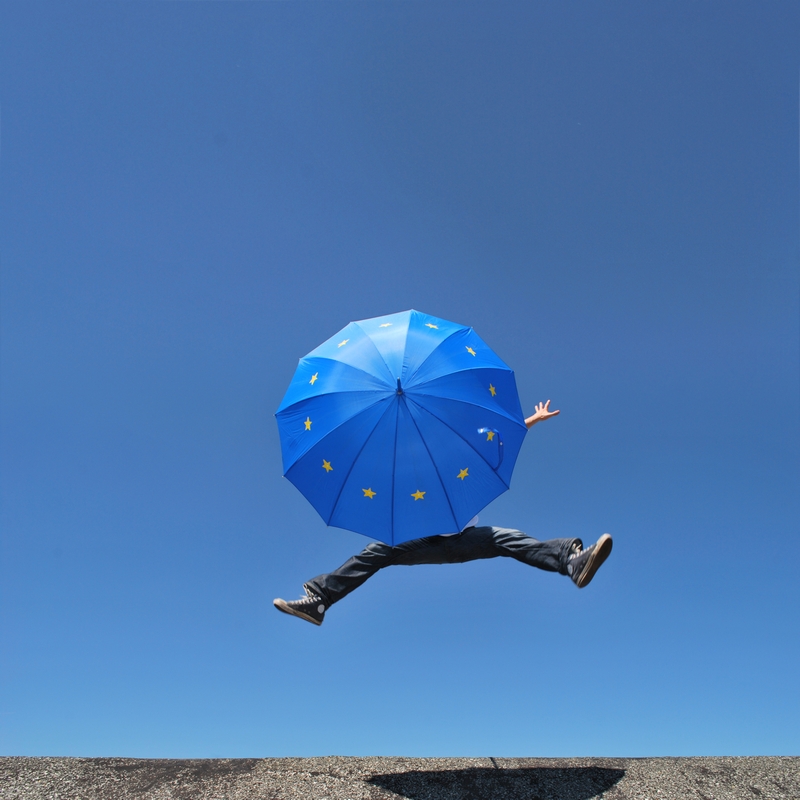 In die Luft springender Mensch mit Schirm, auf der die EU-Flagge zu sehen ist. In die Luft springender Mensch mit Schirm, auf der die EU-Flagge zu sehen ist.