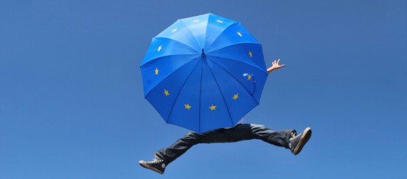 In die Luft springender Mensch mit Schirm, auf der die EU-Flagge zu sehen ist.